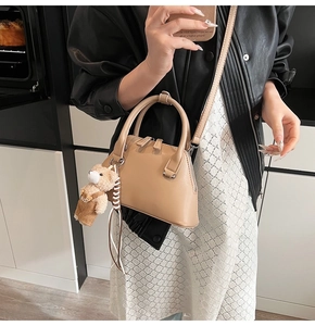 Light beige crossbody bowling bag with plush bear charm shown on a fashion model