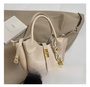 Détail d'un sac seau beige avec fermoir doré et pendentif tissé sur un tissu kaki