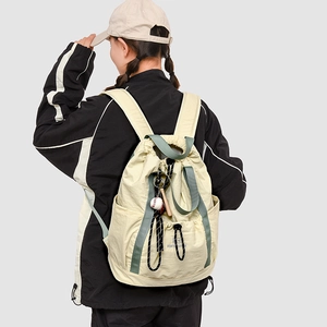 Dettaglio di uno zaino in nylon crema con cinghie verdi e ciondolo a forma di baseball