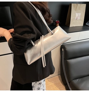 Close-up of metallic silver baguette bag with long tassels on a black suit shoulder