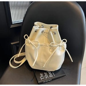 Overhead view of cream white bucket bag with bow knots and metal chain details on a black chair