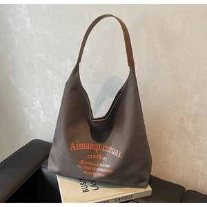 Détail du sac hobo en toile gris foncé avec bandoulière en cuir marron sur canapé