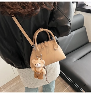 Detail of beige bowling bag with cute bear charm worn as a crossbody bag indoors