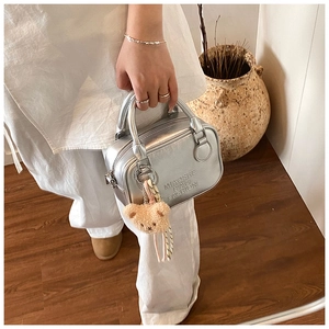Close-up of metallic silver pillow handbag with brand embossing and plush bear charm