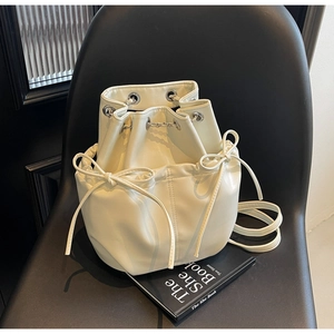 Detail view of a cream white drawstring bucket bag featuring bow accents on a modern chair