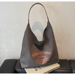 Détail du sac hobo en toile gris foncé avec bandoulière brune sur fauteuil en cuir
