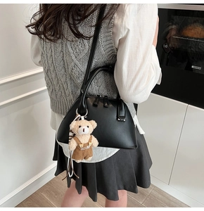 Detail of black bowling bag featuring a cute teddy bear charm on model shoulder