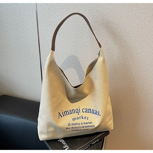 Détail du sac cabas en toile beige avec lettrage bleu artistique et bandoulière en cuir brun