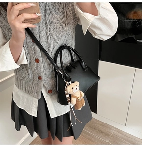 Detail view of black matte leather bowling bag with cute plush bear charm on side