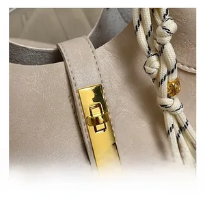 Détail du fermoir doré rotatif et de l'anse tissée sur le sac seau en cuir beige