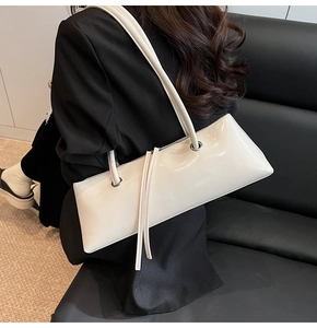 Detail of white baguette bag showing glossy patent leather texture and long tassel zipper pull