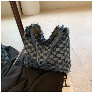 Detail of frayed edges and checkerboard denim texture on a large tote bag with wide straps