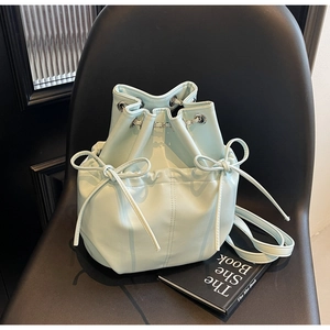 Detail of mint green bucket bag with bow drawstring and silver eyelets on a black chair