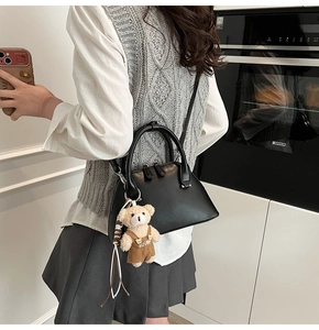 Detail view of a black leather bowling bag featuring a cute brown plush bear charm accessory