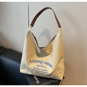 Gros plan du sac fourre-tout beige avec bandoulière en cuir et texte artistique bleu