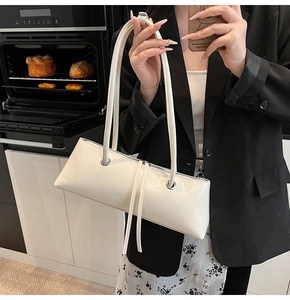 Close-up of beige glossy faux leather baguette bag with silver eyelets and long tassels