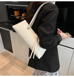 Side view of cream glossy leather baguette bag with fringe detail on model