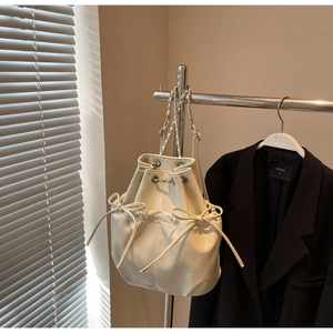 Detail of cream drawstring bucket bag with bow accents and silver chain strap