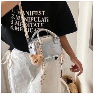 Detail of silver metallic mini handbag with plush bear charm and striped scarf accent