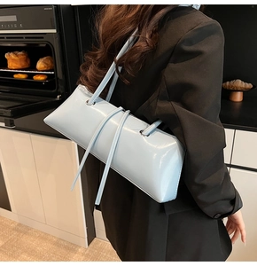 Close-up of a light blue glossy leather baguette bag on a model in a natural kitchen setting