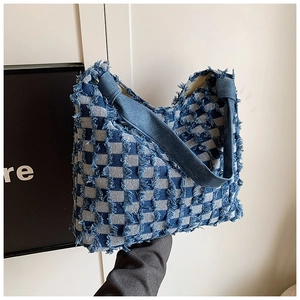 Detail of blue and white checkered denim tote bag featuring frayed edges and fringe texture