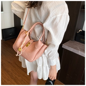 Détail du sac seau en cuir rose avec breloque boule dorée sur une robe blanche