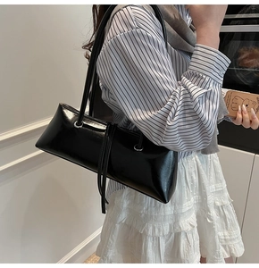 Detail of glossy black patent leather baguette bag with long strap on a shoulder
