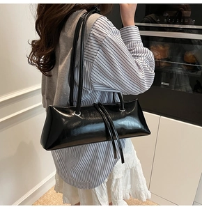 Detail of black glossy baguette bag with silver grommets and slender shoulder straps