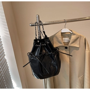 Detail of black drawstring bucket backpack with silver woven chain strap on coat rack