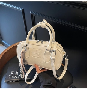 Détail d'un sac bowling blanc cassé avec texture cuir, double poignée et breloque tennis