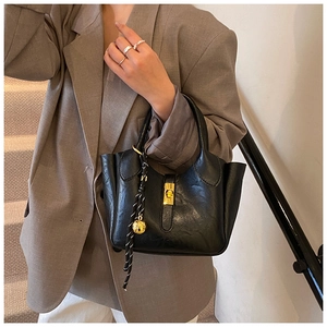 Détail du sac seau en cuir noir avec fermoir doré et poignée décorative en corde tressée