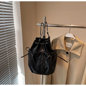 Detail of black leather bucket bag with bow accents and metal chain woven strap