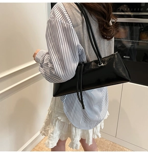 Glossy black baguette bag with long fringe detail worn as a stylish underarm shoulder bag