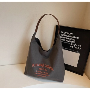 Détail d'un sac cabas en toile grise avec poignées en cuir marron et texte orange