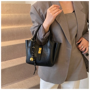 Sac seau noir chic avec fermoir doré porté par un mannequin en costume gris élégant