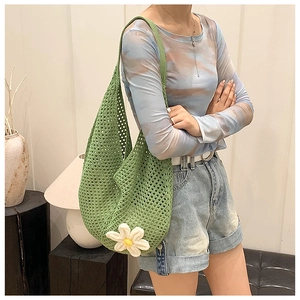 Detail of green knit shoulder bag featuring hollow crochet pattern and white daisy decoration