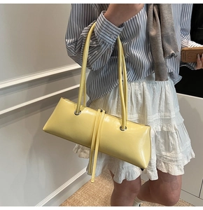 Detail of yellow baguette bag with glossy leather texture and stylish tassel charm