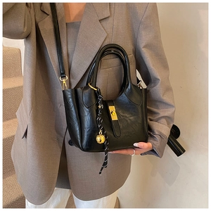 Détail du sac seau noir avec fermoir doré et pendentif sur un costume gris chic