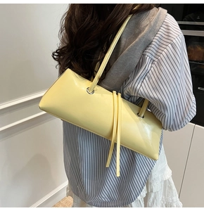 Detail of pale yellow baguette bag featuring side metal eyelets and leather tassel accents