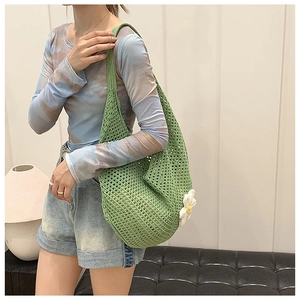 Detail of green woven hollow tote bag featuring a white daisy flower on a knit surface