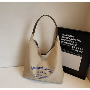 Détail d'un sac fourre-tout en toile crème avec lanières en cuir marron et lettrage bleu