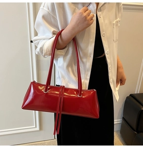 Chic red patent leather baguette bag with long tassels styled on a shoulder