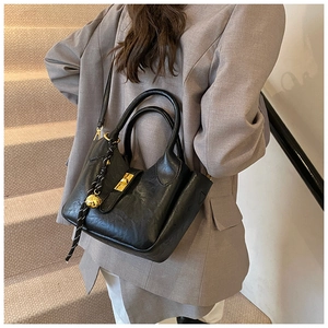 Détail d'un sac seau en cuir noir avec ferrures dorées porté avec un blazer gris