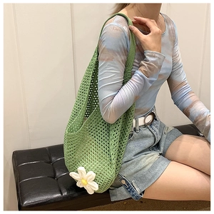 Detail of green woven hollow tote bag with a white daisy charm and crochet mesh texture