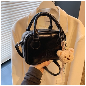 Detail of black glossy pillow bag with embossed lettering and plush bear charm