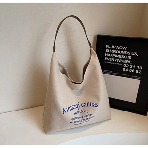 Détail du sac cabas en toile avec lanières en cuir marron et typographie bleue sur table