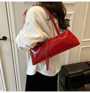 Detail of red glossy patent leather baguette bag with dual shoulder straps and long tassels