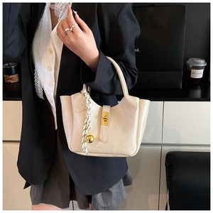 Détail d'un sac seau beige avec finition texturée, fermoir doré et foulard rayé