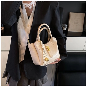 Détail du sac seau beige avec fermoir doré et foulard rayé sur un blazer noir chic