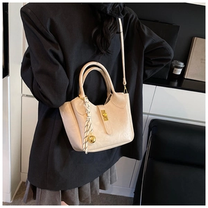 Détail du sac seau beige avec fermoir doré et foulard rayé noir et blanc sur l'anse